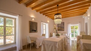 A dining area with wooden beams, white tables, and a chandelier. - Son Simo Vell, Finca 5StarsHome Mallorca (Alcúdia)