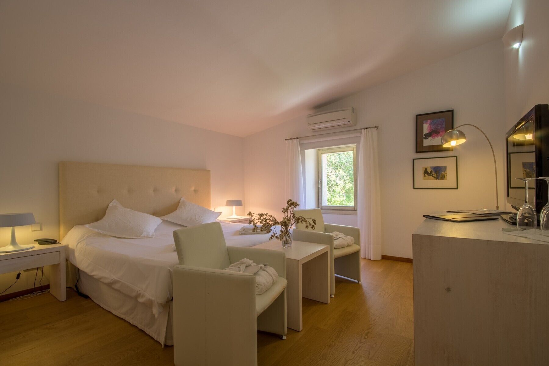 A hotel room with a large bed, two bedside tables, a desk, a chair, a mirror, and a window with curtains.