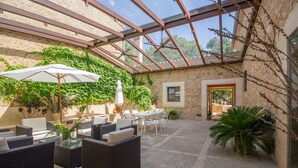 A covered outdoor patio with wicker furniture, a glass ceiling, stone walls, and potted plants. - Son Simo Vell, Finca 5StarsHome Mallorca (Alcúdia)