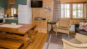 Interior acogedor de una cabaña con paredes de madera, una mesa de comedor, un sofá y una zona de cocina que incluye un refrigerador y un microondas.