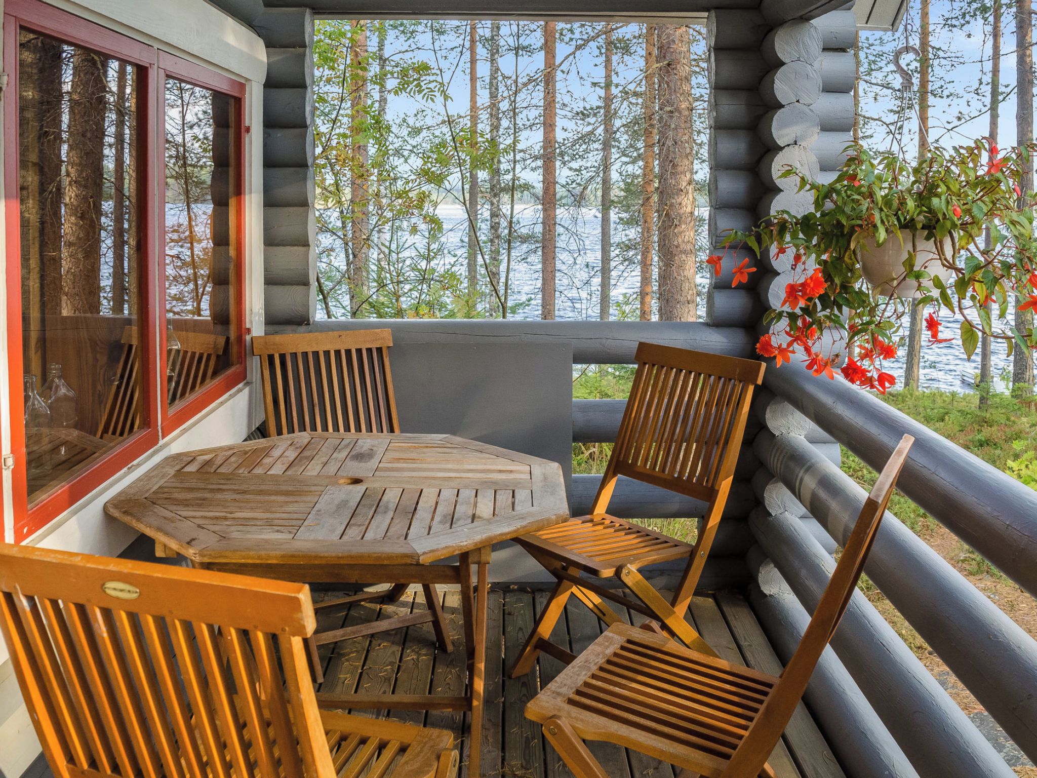 Une table et des chaises en bois sur un balcon, avec vue sur des arbres et une étendue d’eau.