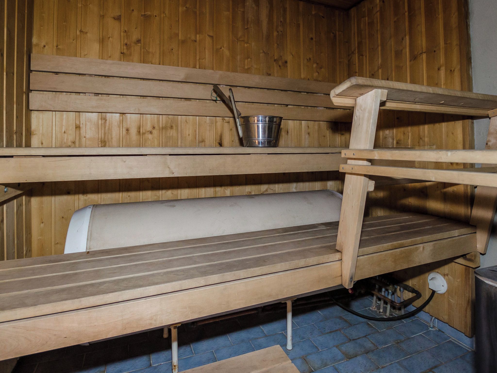 A wooden sauna with benches and a metal bucket.