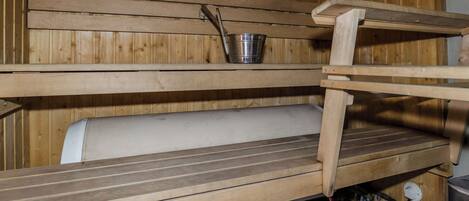 A wooden sauna with benches and a metal bucket.