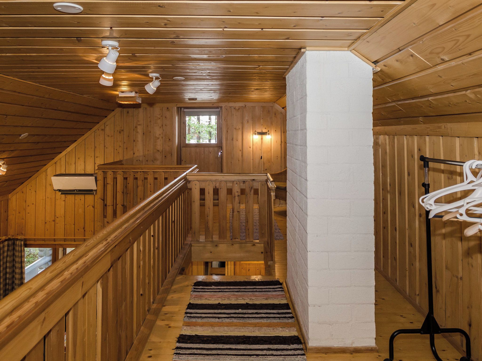 Un escalier en bois avec une rampe, une fenêtre en haut et un mur blanc sur la droite.