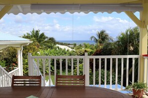 A wooden deck with a bench, white railing, and a view of the ocean and palm trees. - Ti Madinina, a must-see holiday resort with a view of the Diamant rock (LE DIAMANT)