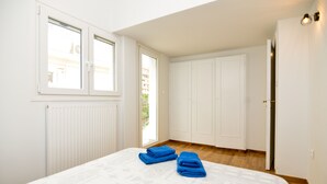 Une chambre avec un grand lit, des murs blancs, une fenêtre et une porte.