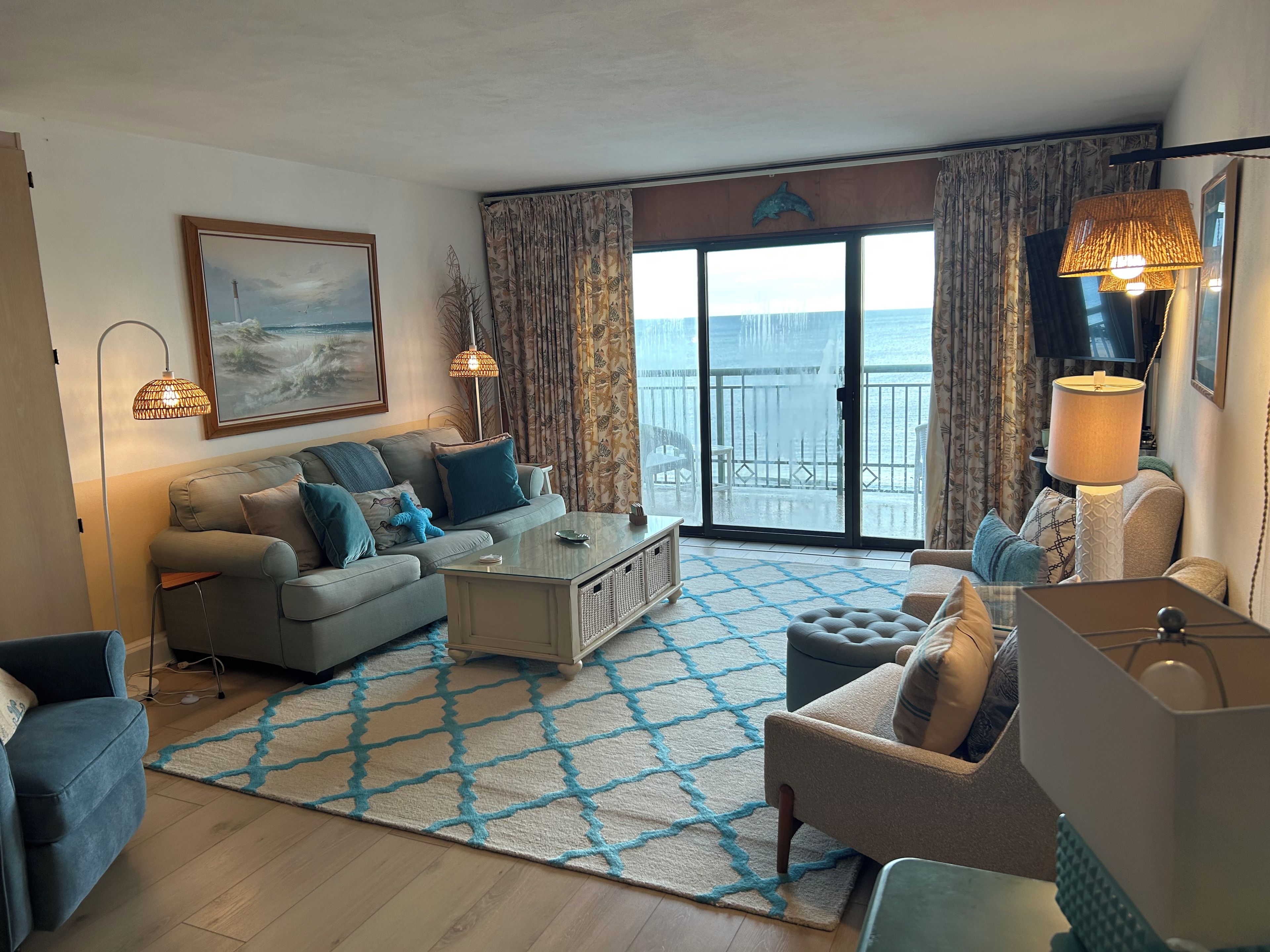 A living room with a sofa, armchairs, a coffee table, and a view of the sea through large windows.