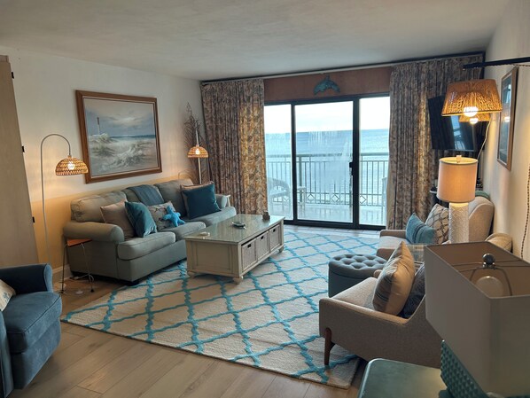 Una sala de estar con sofá, sillones, una mesa de centro y vistas al mar a través de amplios ventanales.