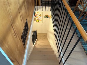 Una escalera de madera con barandilla negra, que conduce a un rellano con una obra enmarcadas.