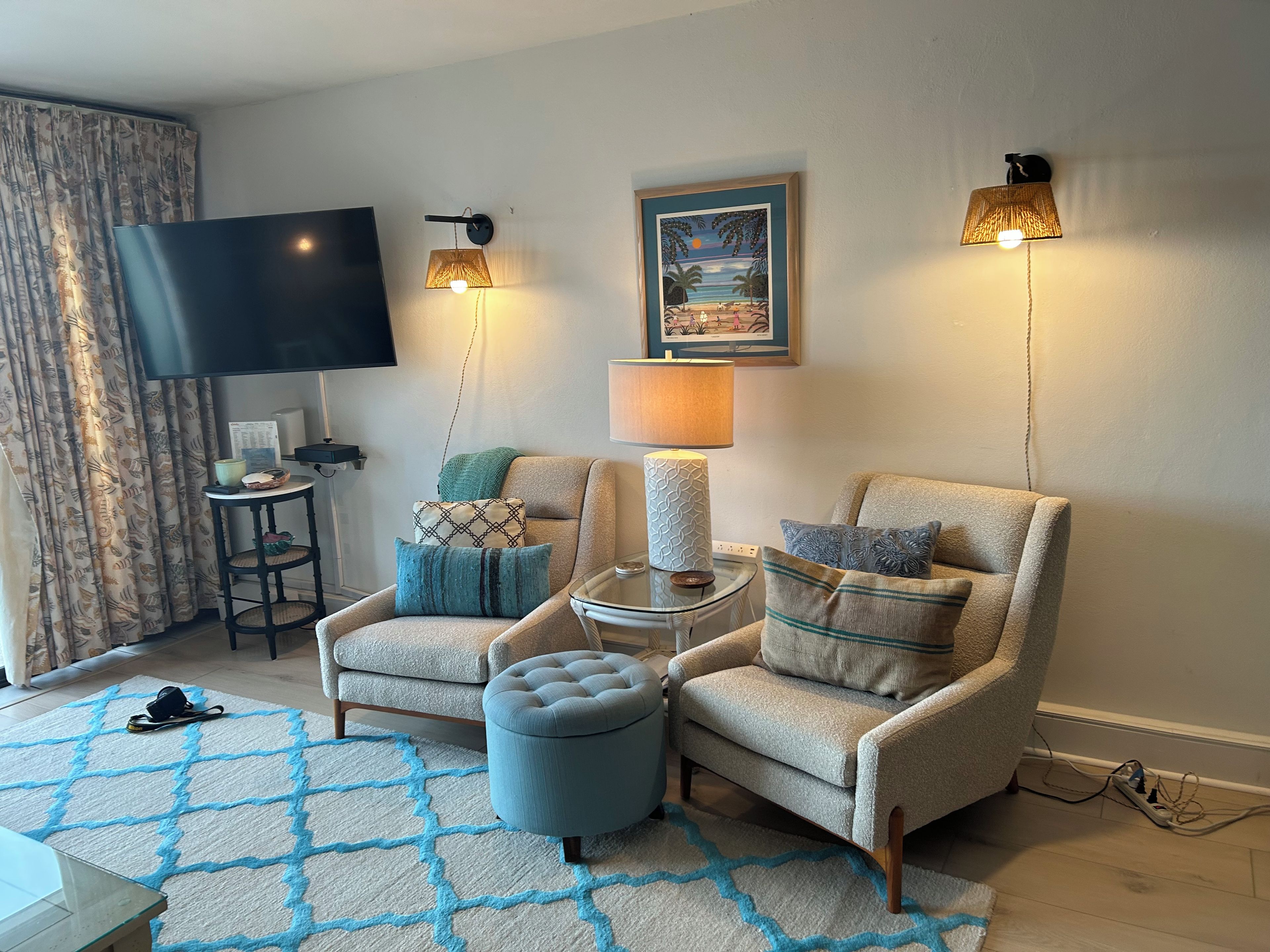 Una sala de estar con dos sillones, una mesa de centro, un televisor y lámparas de pared.