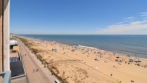A beach with a clear sky, a sandy shore, and a few people walking.
