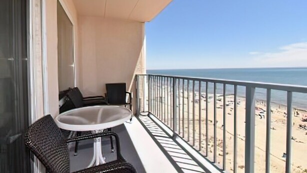 A balcony with a table and chairs, overlooking a beach.