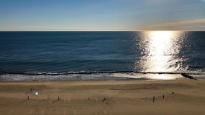 Ein Strand mit blauem Himmel, die Sonne spiegelt sich im Wasser, und Fußspuren führen ins Meer.