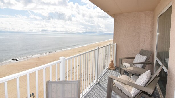 Ein Balkon mit Blick auf den Strand, eine Buddha-Statue und eine Sitzecke mit Kissen.