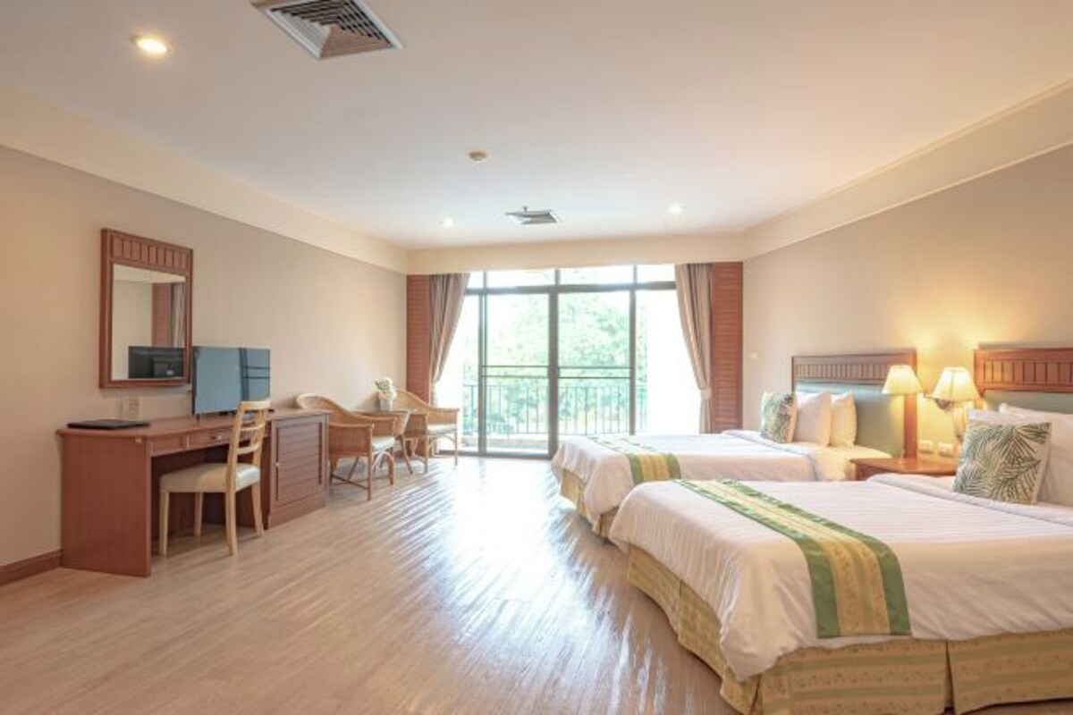 Une chambre d’hôtel avec deux lits, un bureau, une chaise et une grande fenêtre.