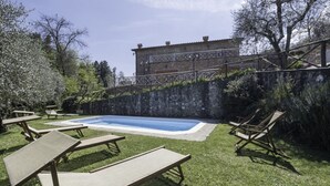 A swimming pool with lounge chairs, a stone wall, and a building in the background.