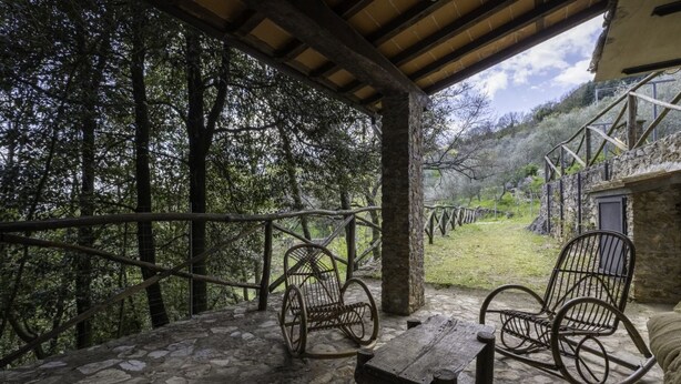 A stone-paved patio with two rocking chairs and a wooden table, overlooking a forested area.