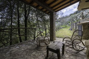 A stone-paved patio with two rocking chairs and a wooden table, overlooking a forested area.