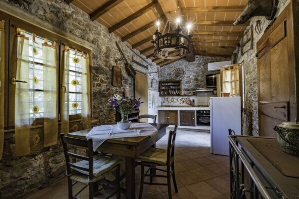 A rustic kitchen with stone walls, wooden beams, and a chandelier.