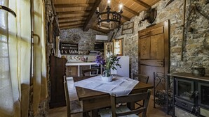 A rustic kitchen with stone walls, wooden beams, a chandelier, and a dining table with chairs.
