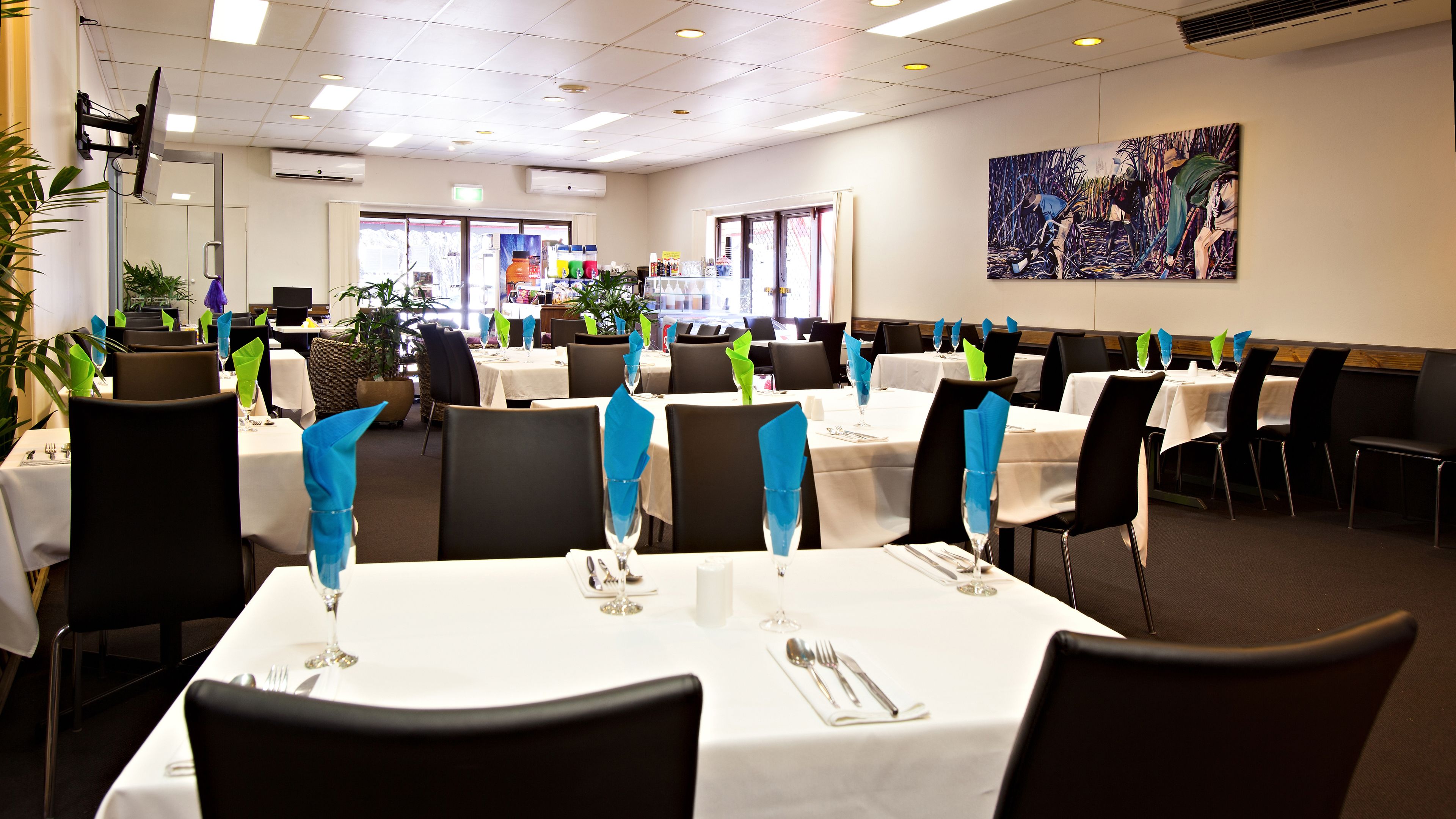 A dining area with tables set for service, featuring blue napkin holders, white tablecloths, and black chairs.