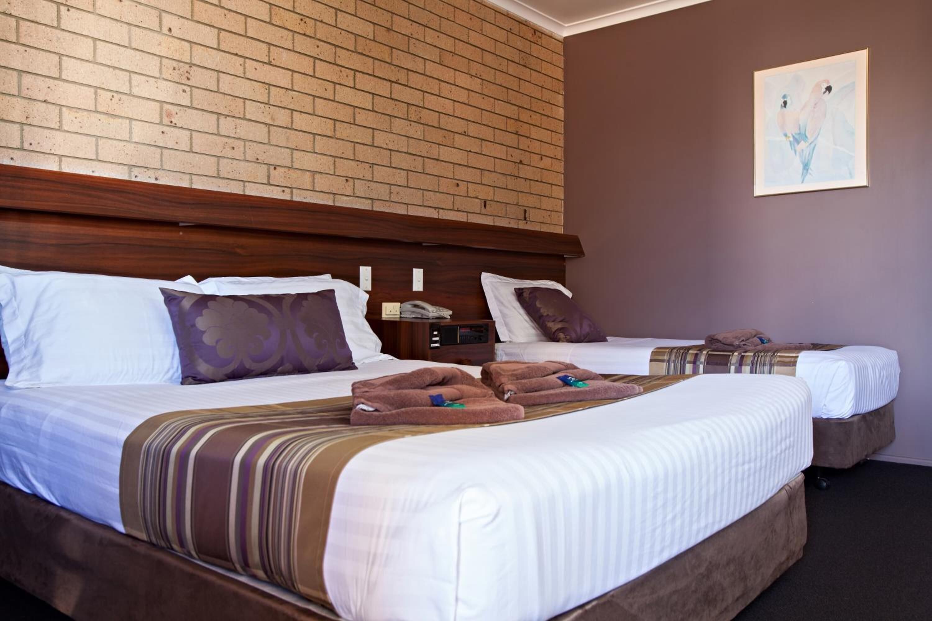 A hotel room with two beds, a brick wall, and a painting.