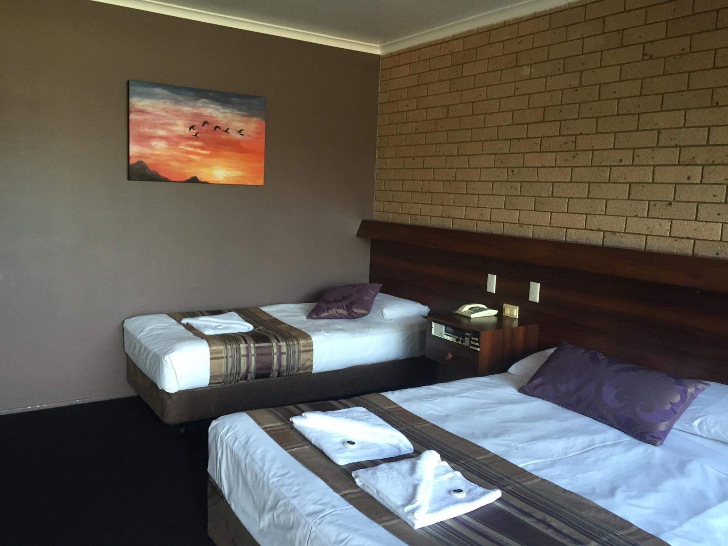 Habitación de hotel con dos camas, una pared de ladrillo y una pintura del atardecer.