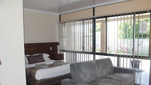 Quarto com cama, sofá cinza e janela com persianas.