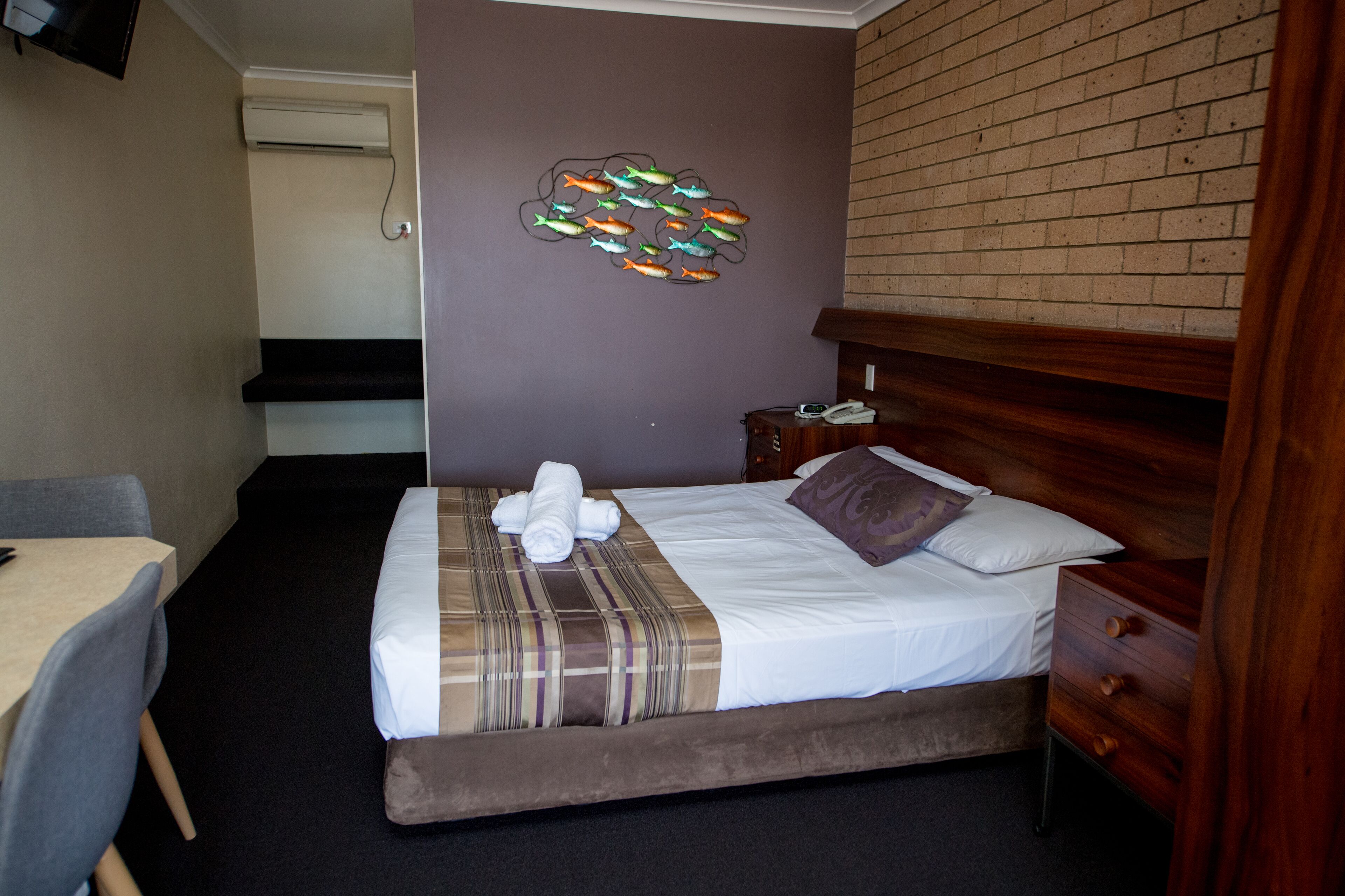 Habitación de hotel con cama, mesita de noche, una silla, escritorio y aire acondicionado de pared.