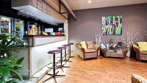Uma área de bar com banquetas, balcão e um espaço de estar com móveis de vime.