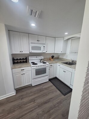 A modern kitchen with white cabinets, a built-in microwave, a stove, and a sink. - OCEAN FRONT CONDO.  ENJOY YOUR MORNING COFFEE SITTING ON YOUR PRIVATE BALCONY WATCHING THE SUNRISE. (Rehoboth Beach)