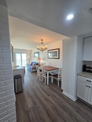 A modern kitchen with white cabinets, a wooden dining table, and a chandelier.