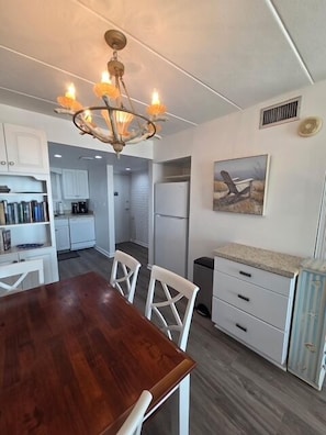 A modern kitchen with white cabinets, a wooden dining table, and a chandelier. - OCEAN FRONT CONDO.  ENJOY YOUR MORNING COFFEE SITTING ON YOUR PRIVATE BALCONY WATCHING THE SUNRISE. (Rehoboth Beach)