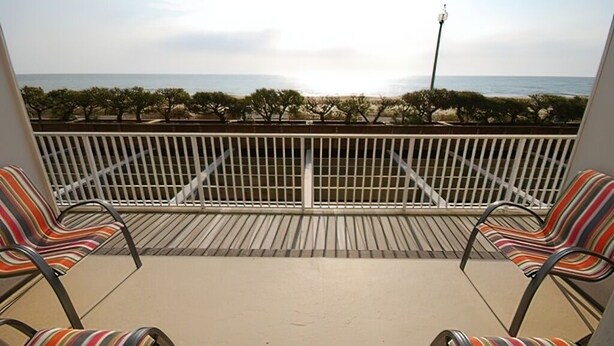 A balcony with two striped chairs facing a beach and ocean view. - WALK RIGHT ONTO THE BOARDWALK FROM APARTMENT PATIO! (Rehoboth Beach)