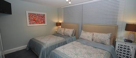 A bedroom with two beds, a TV, a painting, and a nightstand with a lamp.