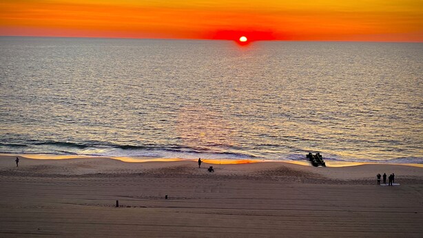 Una spiaggia al tramonto, con mare calmo e persone che pescano.