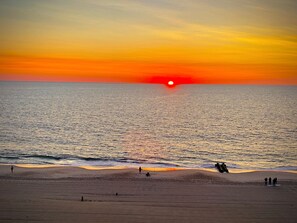 A beach with a sunset, calm sea, and people fishing. - OCEAN FRONT CONDO.  ENJOY YOUR MORNING COFFEE SITTING ON YOUR PRIVATE BALCONY WATCHING THE SUNRISE. (Rehoboth Beach)