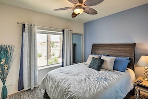 A bedroom with a bed, a ceiling fan, a window with curtains, and a nightstand with a lamp. - Elegant Lake Havasu Getaway w/ Pool - 3 Mi to Lake (Lake Havasu City)