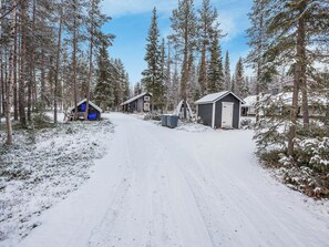 A snow-covered road leading to a cabin area with multiple buildings, including a small shed and a larger cabin with a door. - Vacation home  by Interhome (Äkäslompolo)