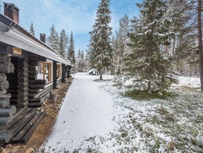 A log cabin with a snow-covered path leading to it, surrounded by tall pine trees. - Vacation home  by Interhome (Äkäslompolo)