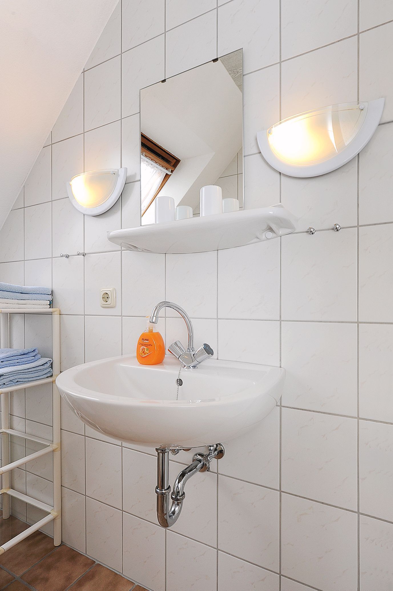 Un bagno con un lavandino bianco, uno specchio e due luci a parete.