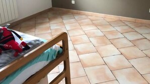 Una habitación con una cama de madera, un radiador, un ventanal y piso de baldosas.
