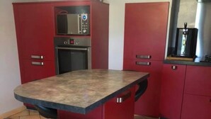 Una cocina con armarios rojos, un microondas y un taburete de bar.