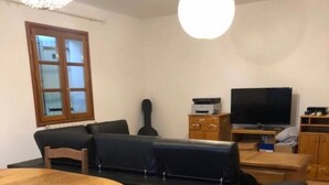 Una sala de estar con una mesa redonda de madera, un sofá negro, un televisor y una guitarra.