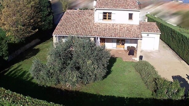 Una casa de dos pisos con techo de tejas, rodeada de jardines y setos bien cuidados.