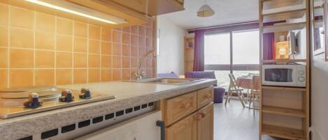 A compact kitchen with wooden cabinets, a granite countertop, a microwave, and a window overlooking a balcony.