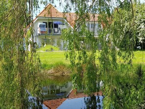 Ein Haus mit Ziegeldach, einem Balkon und einem Teich im Vordergrund.