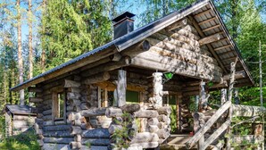Une cabane rustique en rondins de bois, dotée d’un porche et d’un escalier menant à l’entrée.