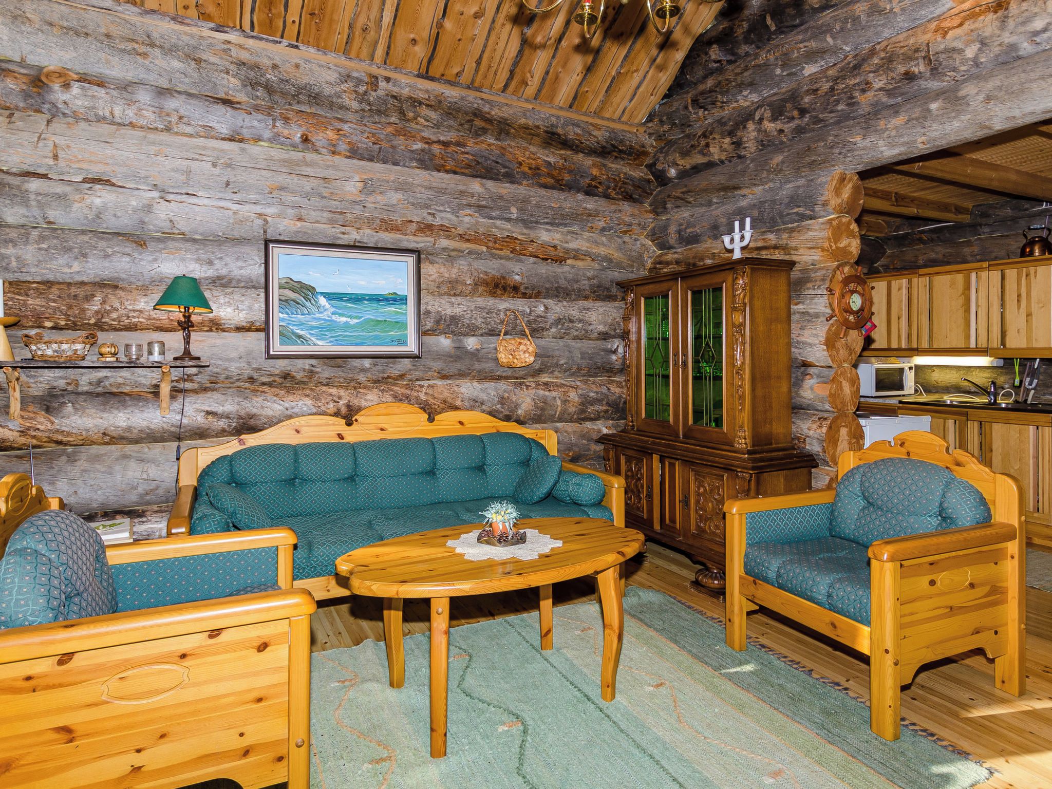 A log cabin interior with a wooden sofa, armchairs, a dining table, and a kitchen area.