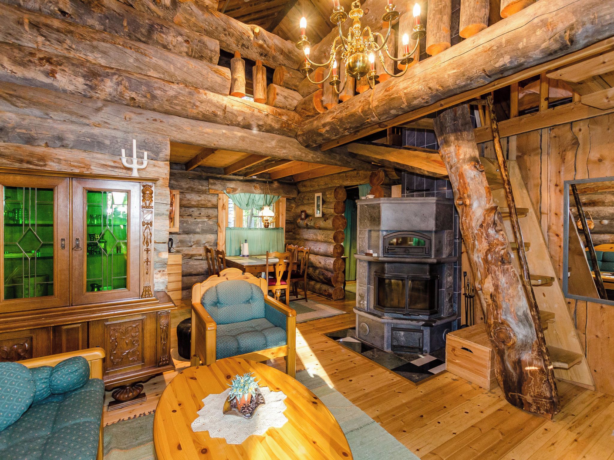 A rustic cabin interior with a stone fireplace, wooden furniture, and a chandelier.